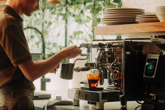 Person operating a high end espresso machine to prepare coffee at home with a steaming wand