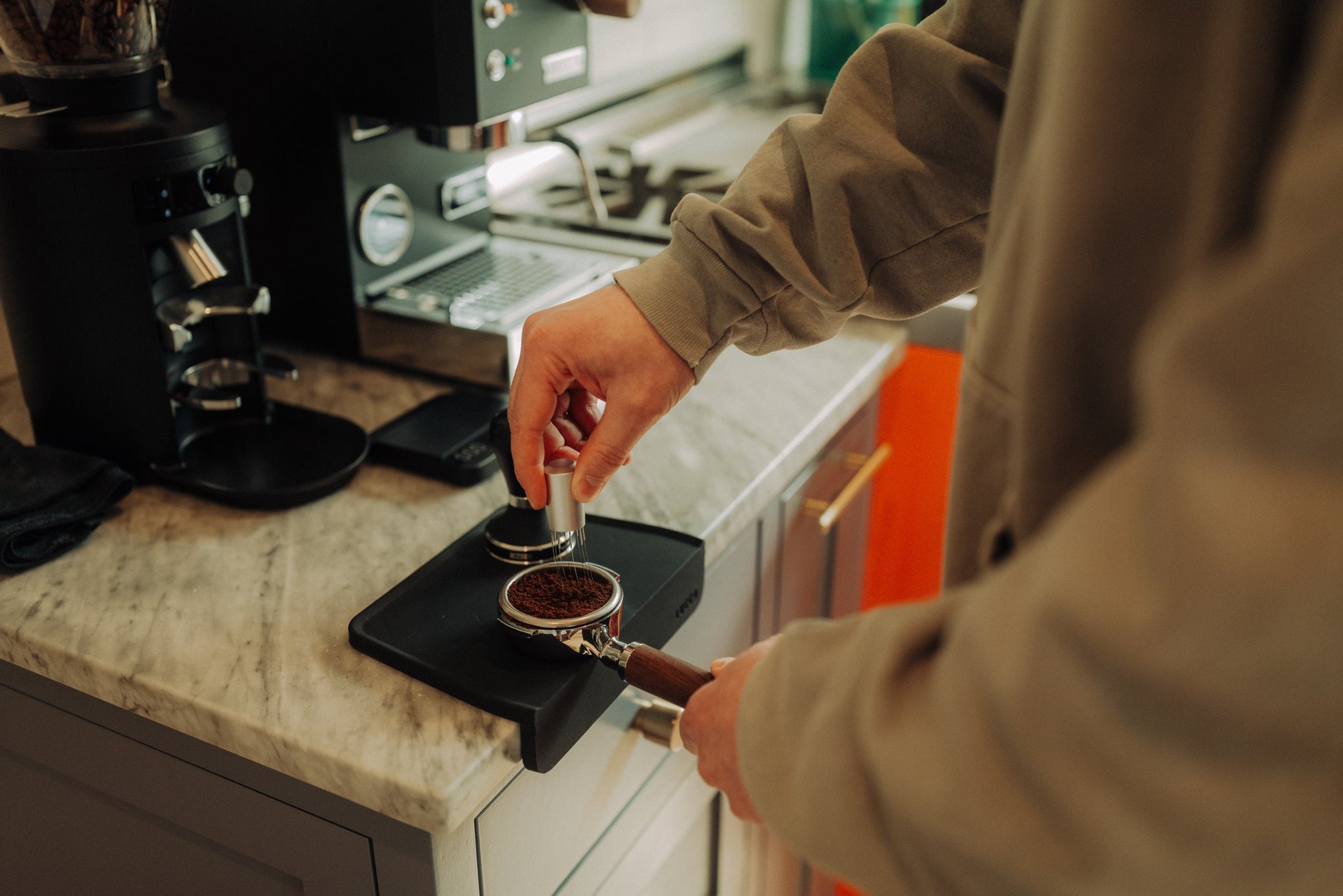 Close up of hands loading ground coffee into a portafilter on a home espresso machine