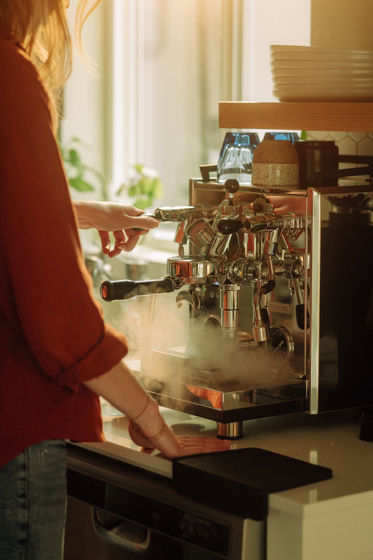 Barista adjusting a blue Profitec espresso machine with chrome group heads in a bright cafe