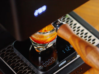 Espresso pouring into a glass from a lever espresso machine with a wooden handle