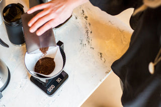 Beginner coffee brewing setup with ground coffee in a cone filter over a glass carafe on a marble countertop