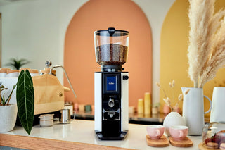 Anfim Luna espresso grinder with a glass bean hopper filled with coffee beans on a bright kitchen counter.