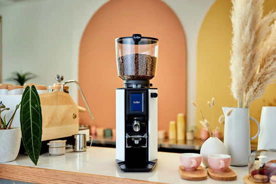 Anfim Luna espresso grinder with a glass bean hopper filled with coffee beans on a bright kitchen counter.
