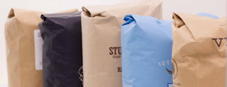 Row of assorted coffee bags in beige black and blue standing upright.