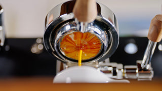 Close up of a polished chrome espresso machine group head with a wooden handle portafilter