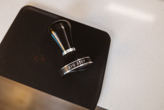 Close up of a coffee tamper resting on a dark surface with a blurred backdrop