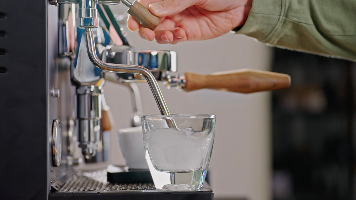 Barista hand turning a wooden lever on a professional espresso machine over a glass