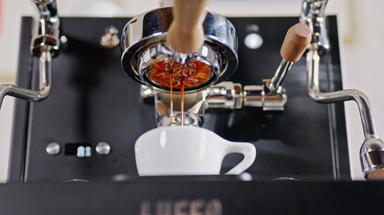 Espresso pours from the portafilter into a white cup on a professional machine.