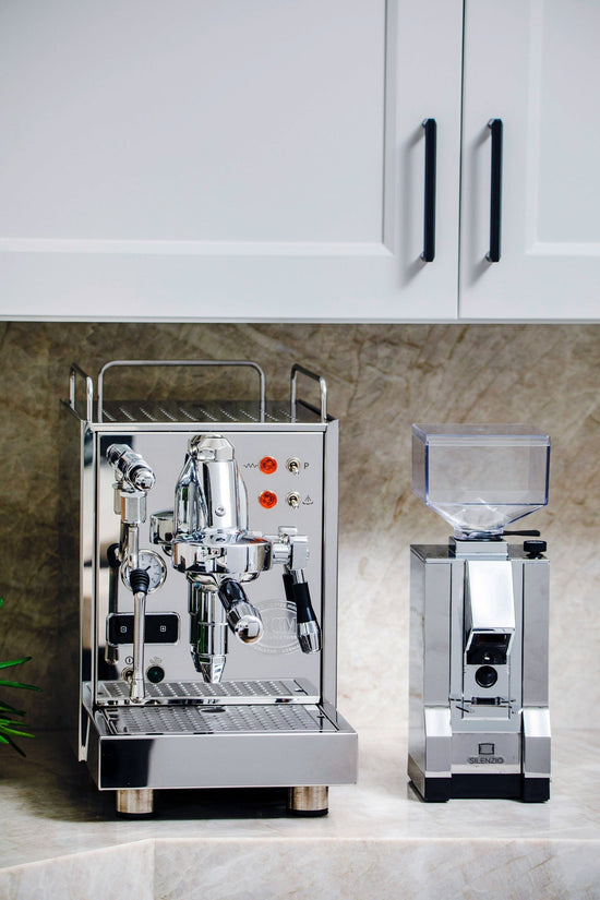 White kitchen cabinets with black bar handles above a stainless espresso machine on a marble countertop.