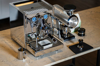 Polished stainless espresso machine with two group heads and blue gauges on a marble countertop