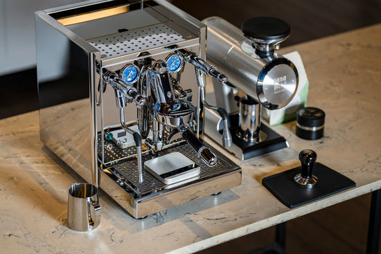 Polished stainless espresso machine with two group heads and blue gauges on a marble countertop