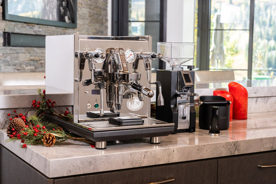 Dual group head stainless espresso machine on a marble counter with festive greenery and pine cones