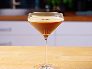 Espresso martini in a coupe glass with coffee bean garnish on a wooden counter