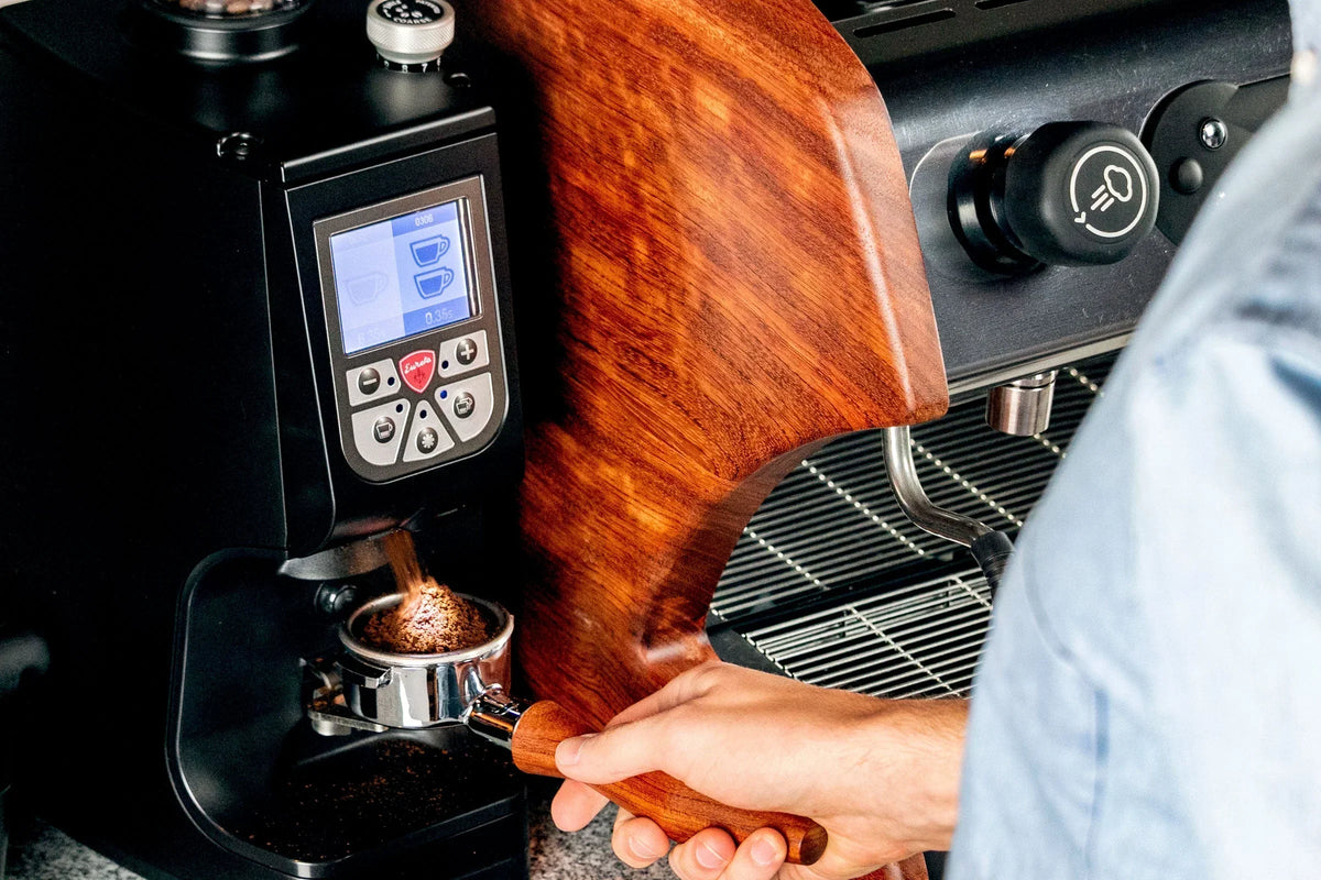 Close up of Eureka Atom 75 espresso grinder with wood side panel and a barista's hands near the portafilter.