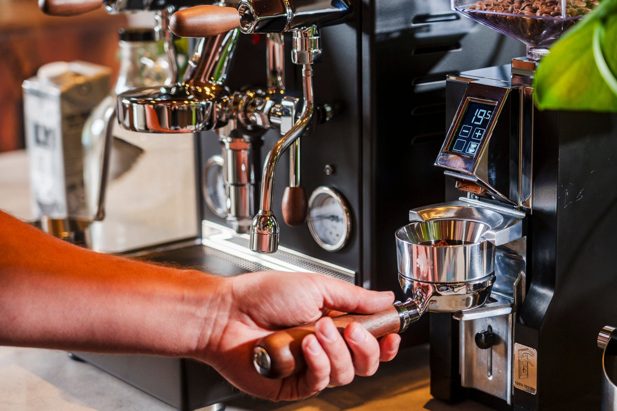 Close up of hands tamping espresso into a portafilter mounted on a high end home espresso machine.