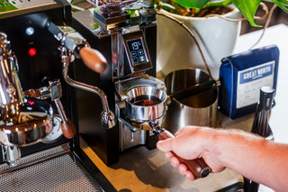 Close-up of a hand holding a portafilter under a shiny espresso machine with a bean hopper above