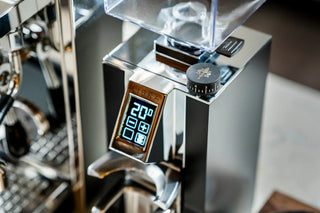 Close up of a shiny espresso grinder showing a large dial and blue digital readout for grind settings.