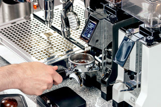 Barista inserts a portafilter into a polished espresso machine with a digital display.