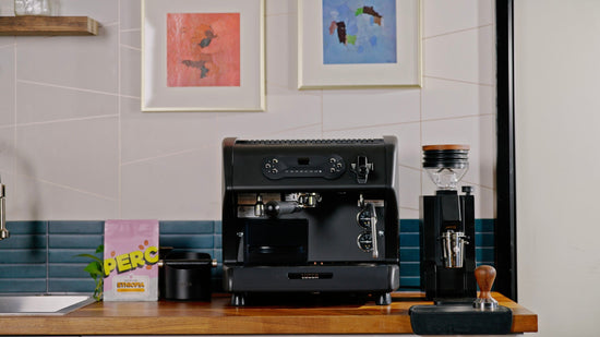 Home coffee setup showing a black espresso machine on a wooden counter with a grinder on the right and an Ethiopian coffee bag on the left.