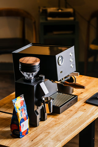 Espresso machine with a portafilter attached and a bag of coffee on a wooden counter.