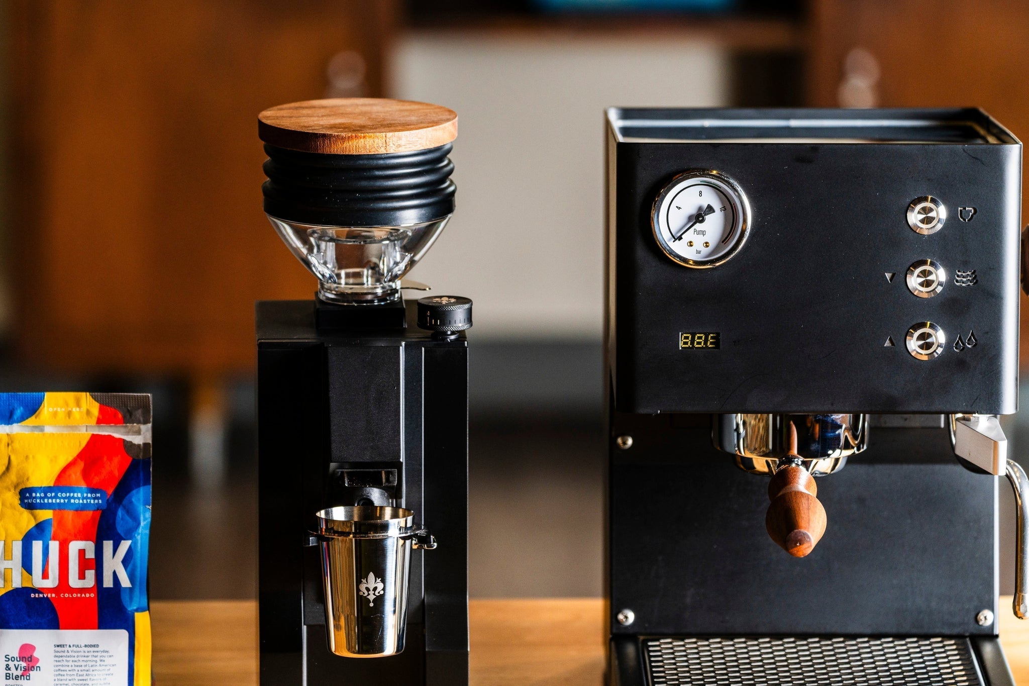 Close up view of the Eureka Zero Mignon Zero 65 Espresso grinder in matte black sitting to the left of a matte black LUCCA Tempo espresso mahcine lifestyle by Clive Coffee