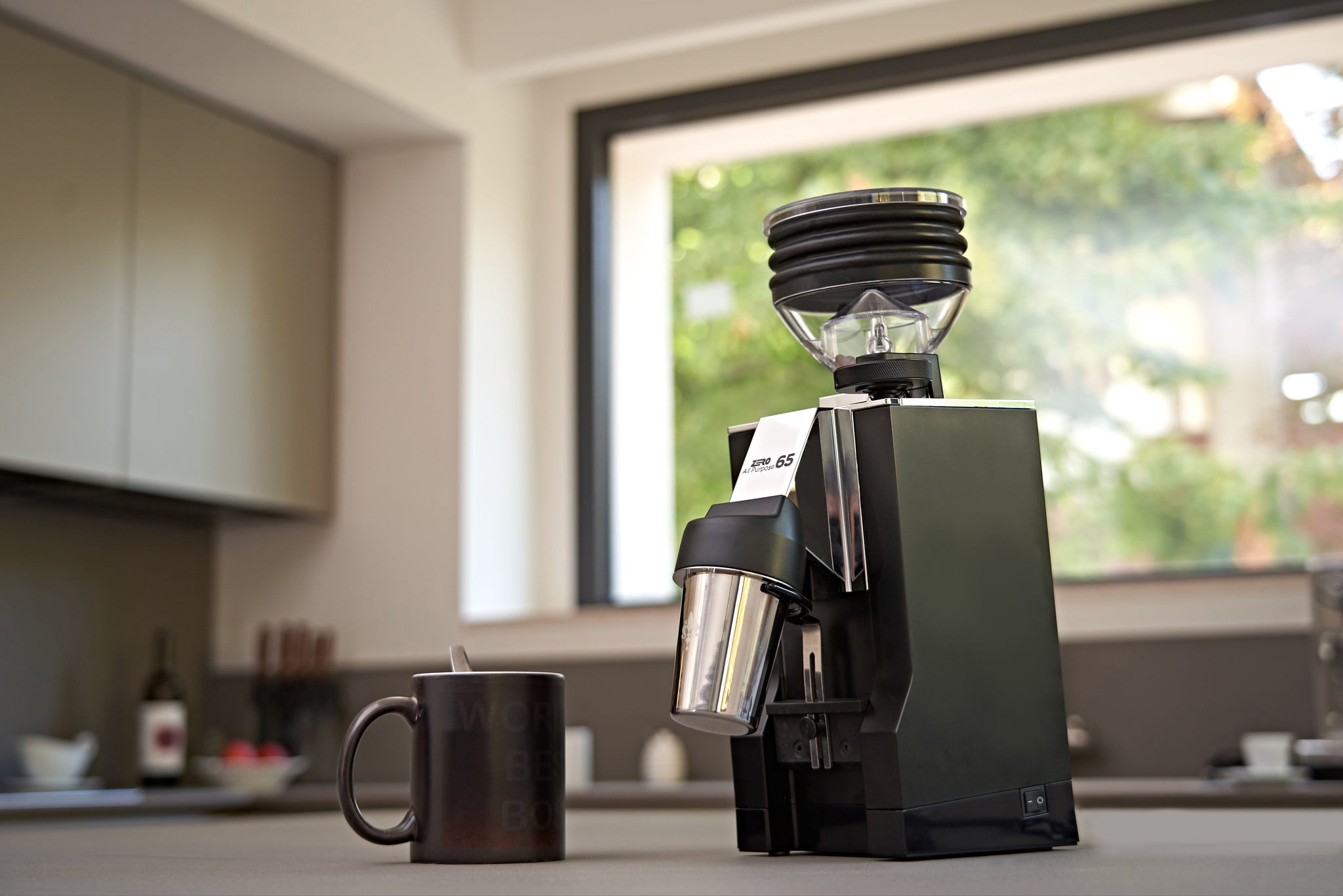 Close up of a professional coffee grinder with a large black hopper and chrome body on a kitchen counter