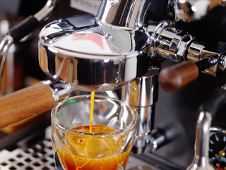 Close up of a chrome espresso machine pouring espresso into a glass with crema
