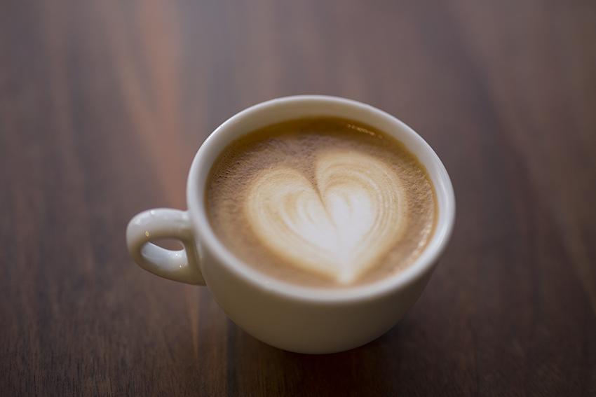 White ceramic cup of latte with a heart shaped foam design on a wooden surface.