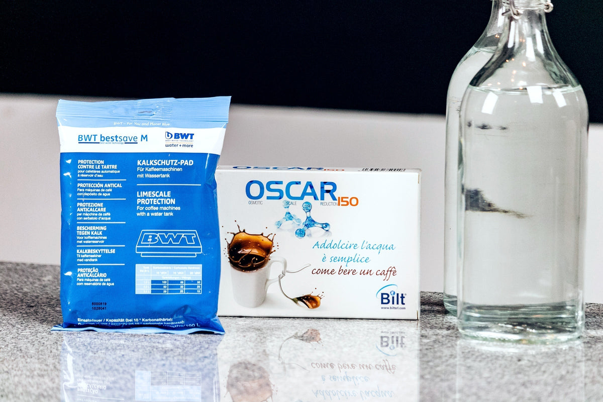 Blue BWT water filter packaging beside an Oscar water treatment box on a kitchen counter next to a glass bottle