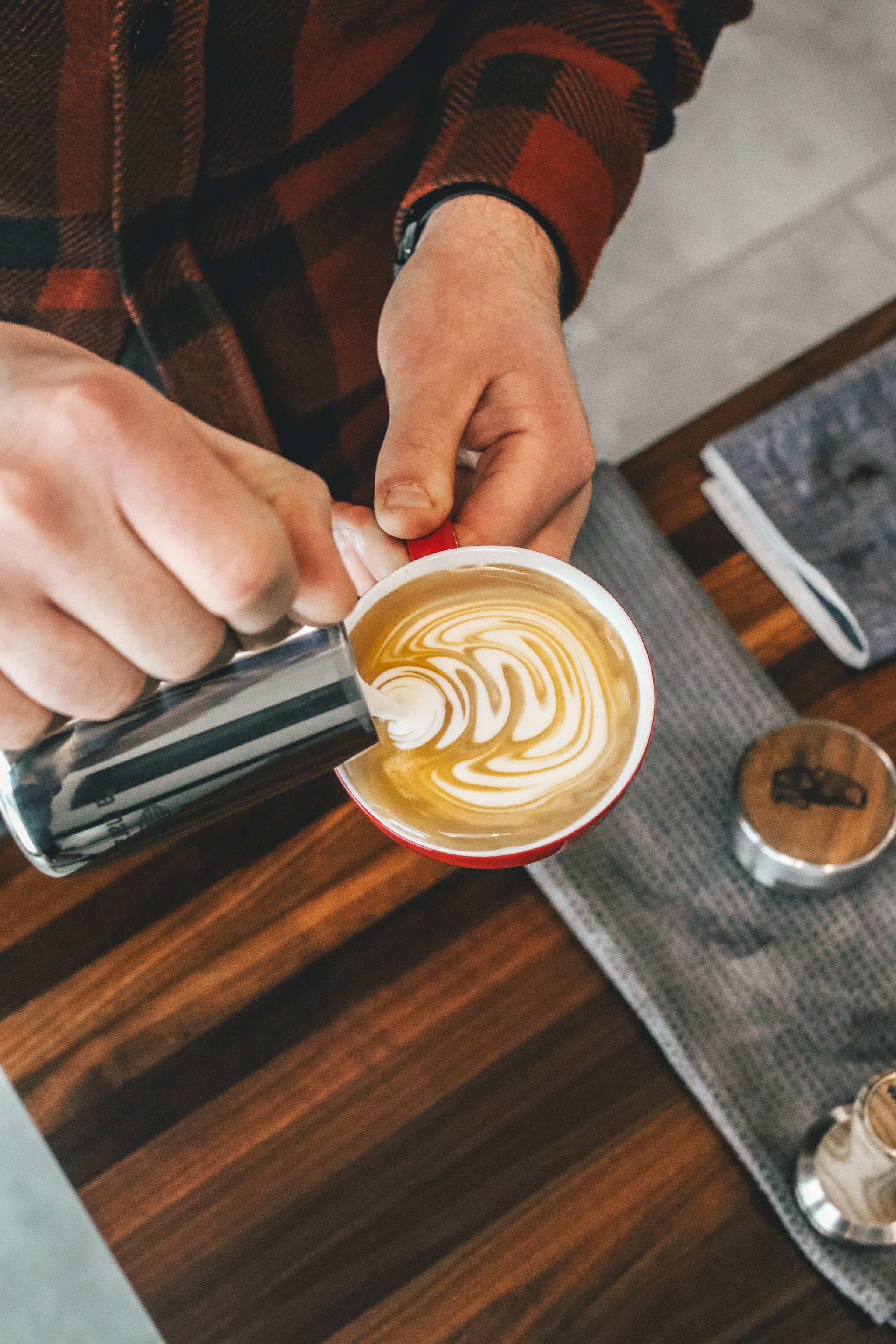 Barista pours steamed milk to create glossy latte art in a red cup.
