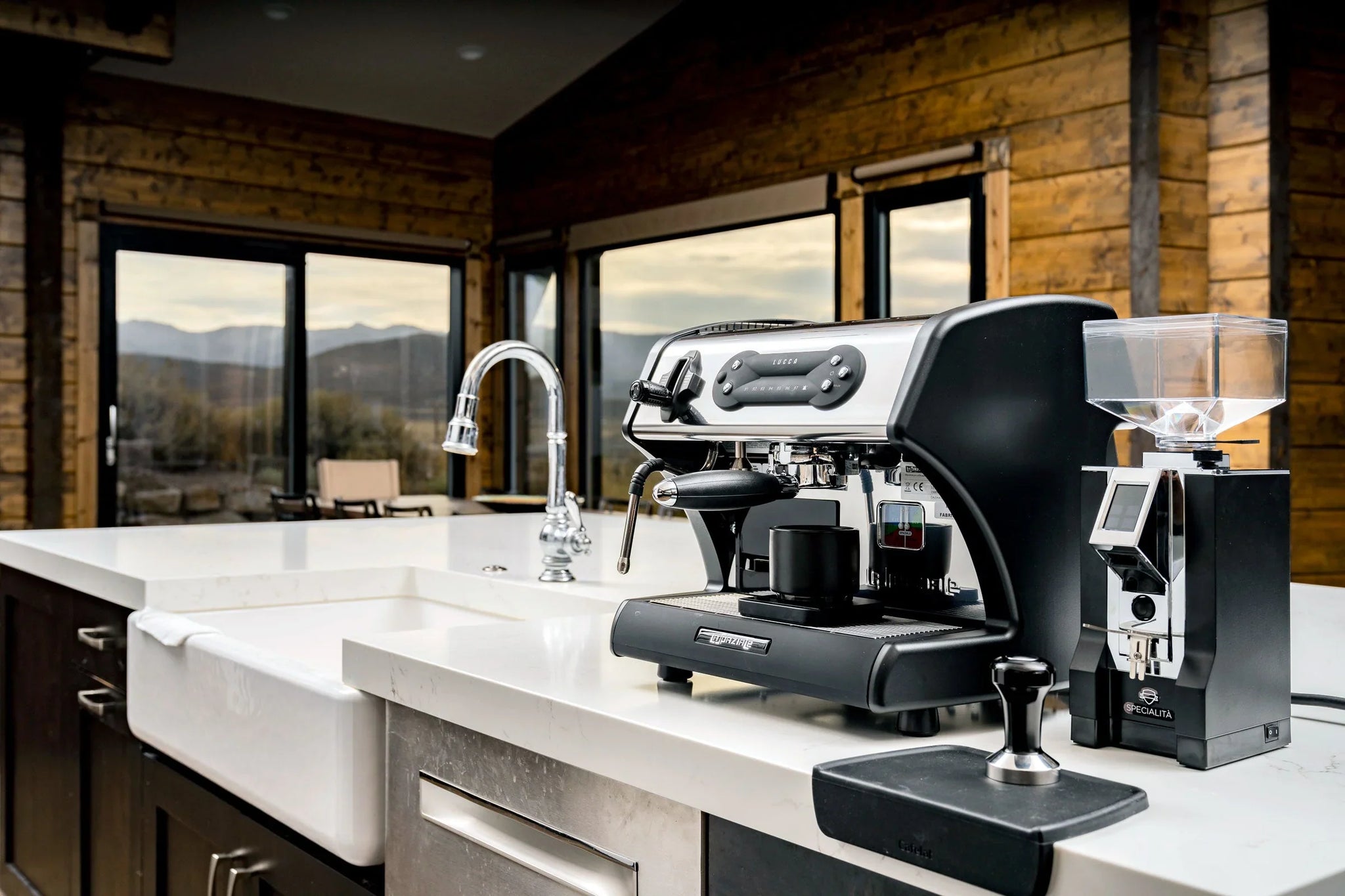 Stainless espresso machine with portafilter and steam wand sits on a white countertop in a warm wood kitchen.