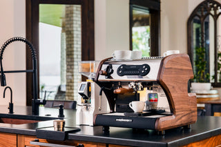 Professional espresso machine with wood side panel on a kitchen counter and cups on top
