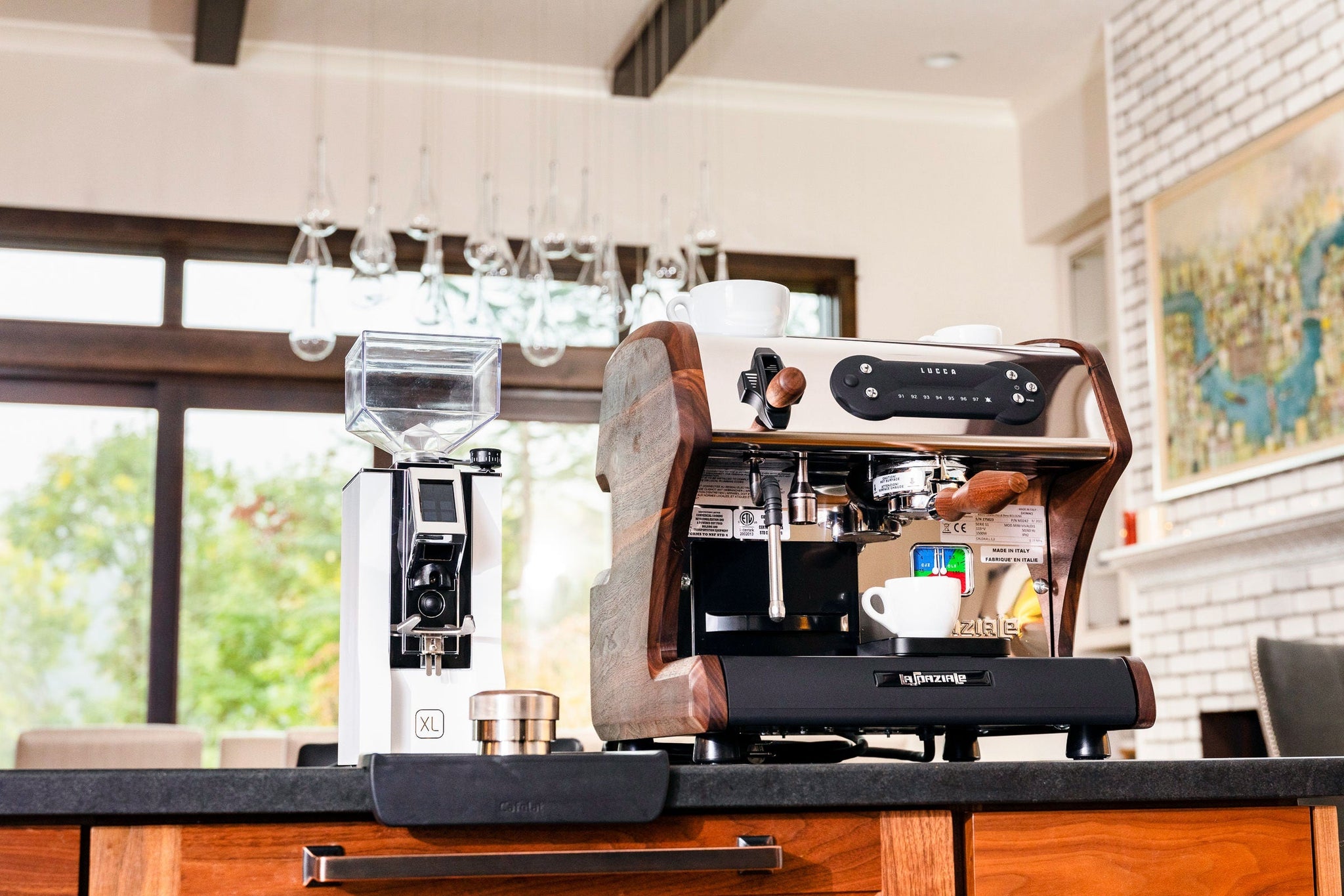 Wood trimmed espresso machine with a white cup on top and a coffee grinder beside it in a bright cafe