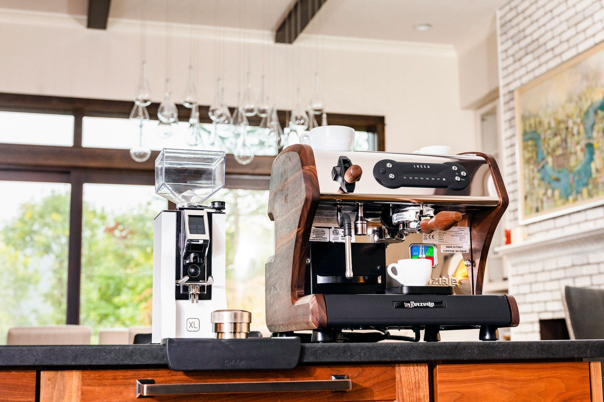 Gourmet home espresso setup with a polished lever machine on the right and a tall silver grinder on the left on a marble counter.