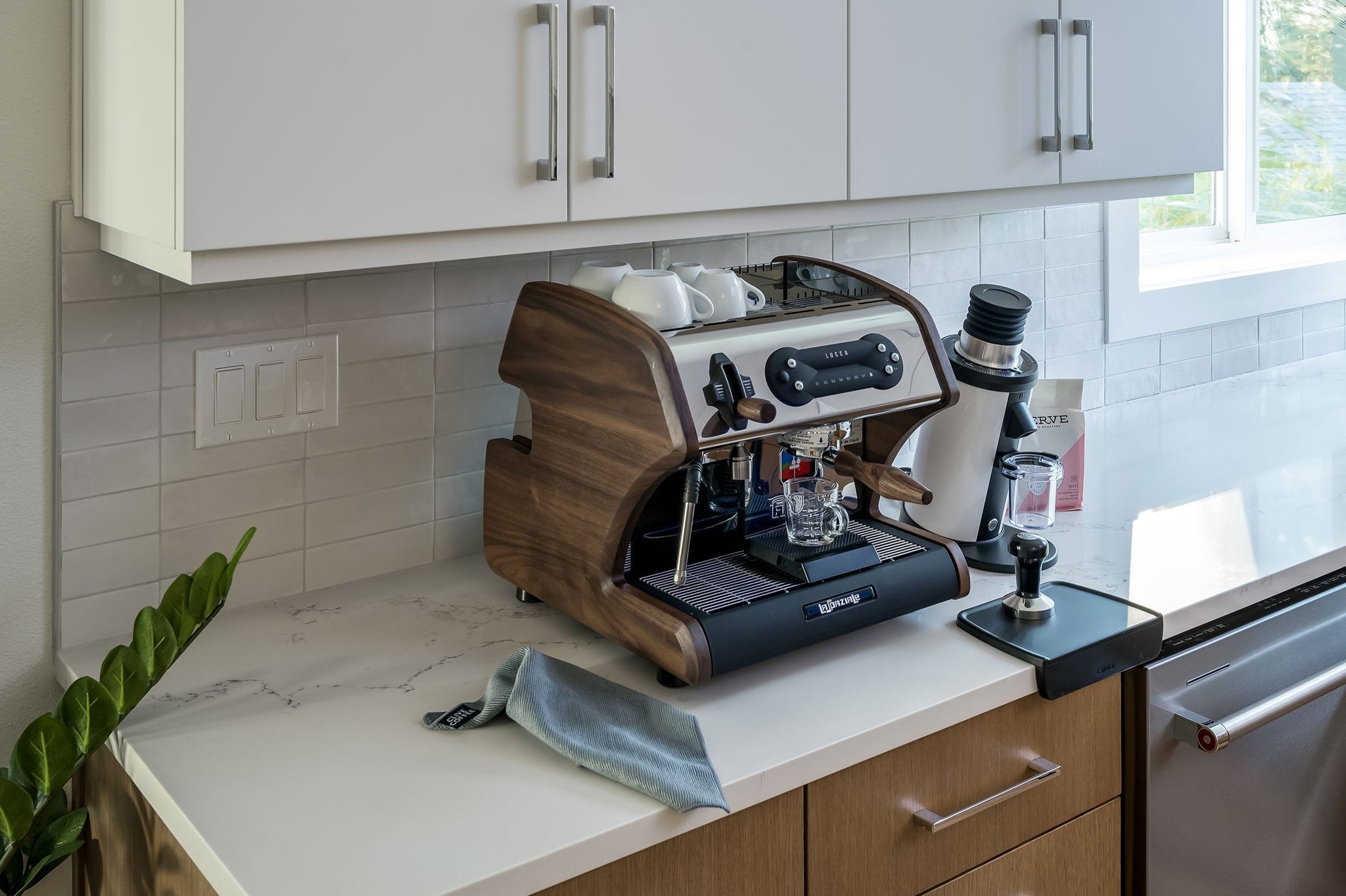 LUCCA espresso machine with wooden side panels on a marble kitchen counter beneath white cabinets.