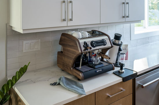 LUCCA espresso machine with wooden side panels on a marble kitchen counter beneath white cabinets.