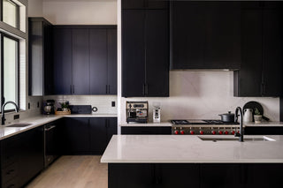 Wide shot of a modern kitchen with dark cabinets, marble countertops and stainless appliances