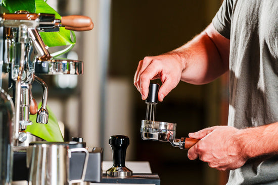 Barista hands operate a bottomless portafilter under an espresso machine during extraction.