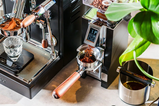 Close up of a high end espresso setup with a wooden handle portafilter and a bean hopper.