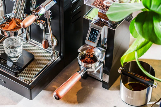 Close up of a polished espresso machine with a portafilter that has a wooden handle and ground coffee visible in the dosing area.