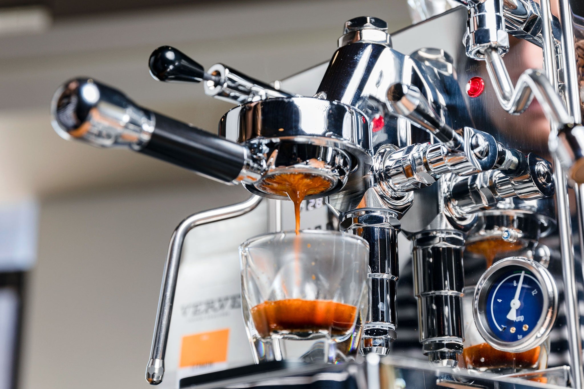 Close-up of a chrome espresso machine with a portafilter dripping espresso into a clear glass cup.