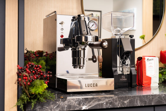 Commercial espresso machine with chrome body and gauge beside a grinder with a clear hopper in a showroom