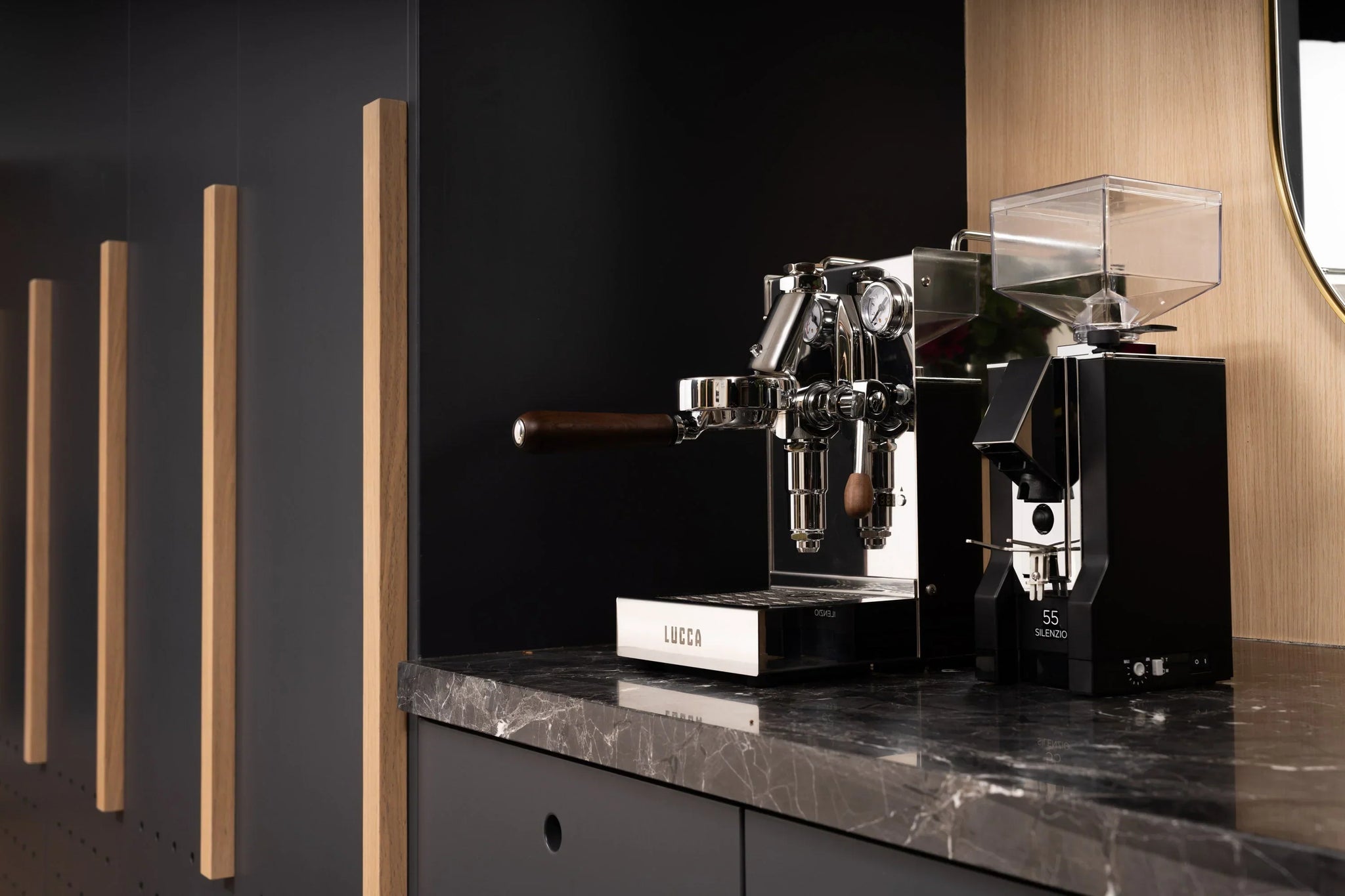 Modern coffee setup featuring LUCCA espresso machine and grinder on a wooden table with framed abstract art above and a bag of HUCK coffee nearby