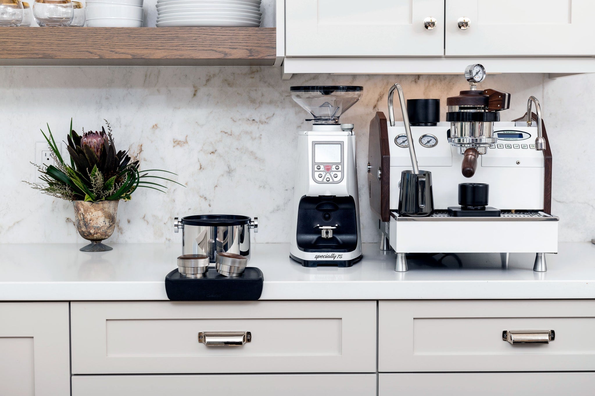 Bright kitchen counter with a commercial espresso machine, grinder, and scale among white cabinets