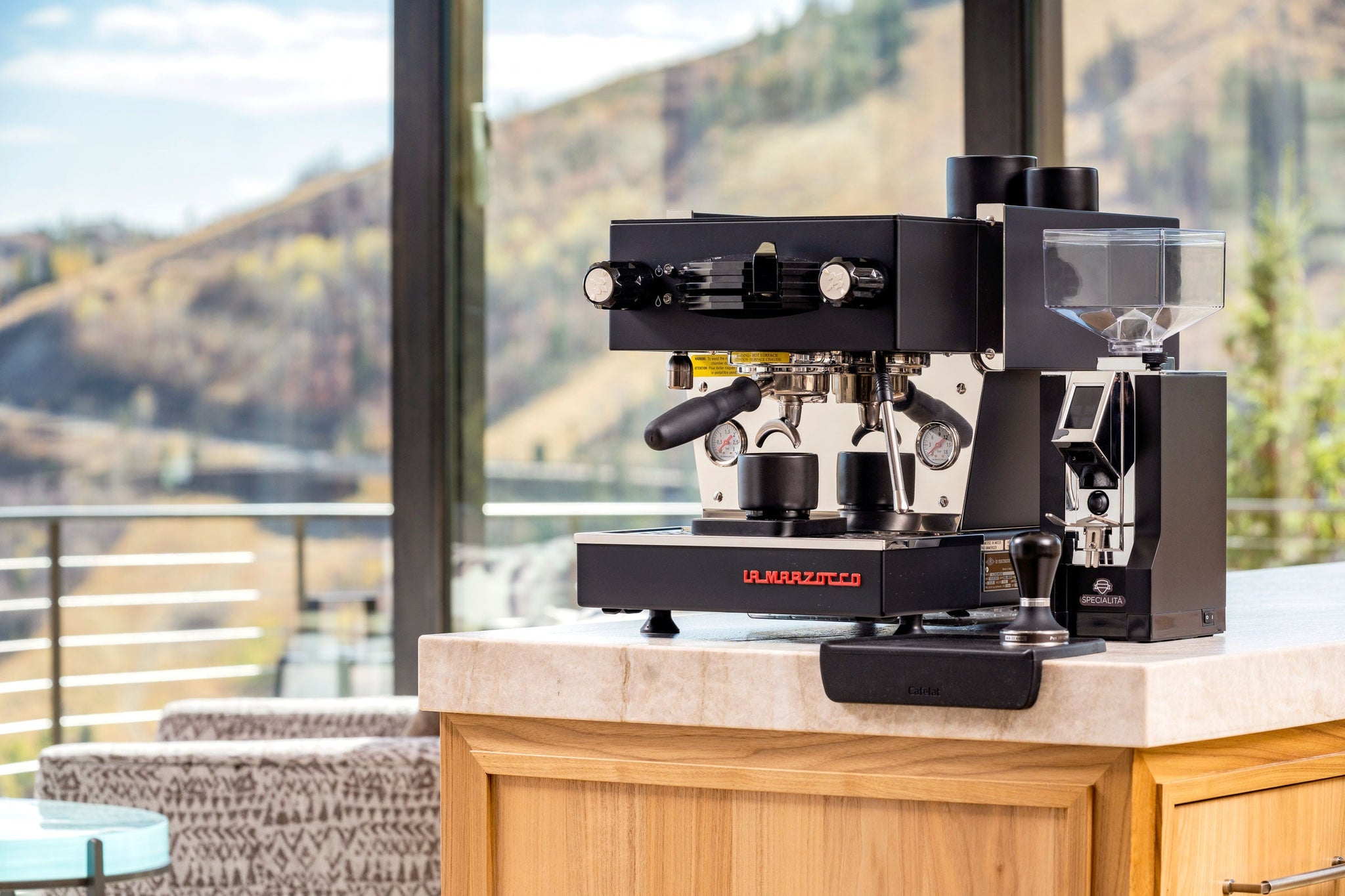 La Marzocco espresso machine with portafilter on a counter by a window overlooking hills