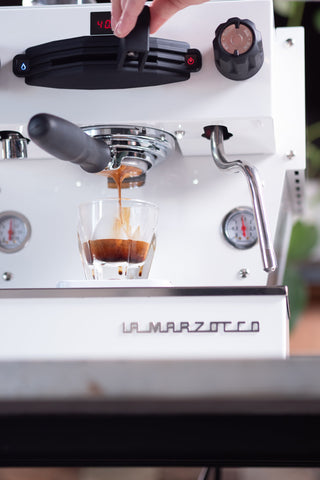 La Marzocco home espresso machine in white finishes brewing a shot into a glass with crema.