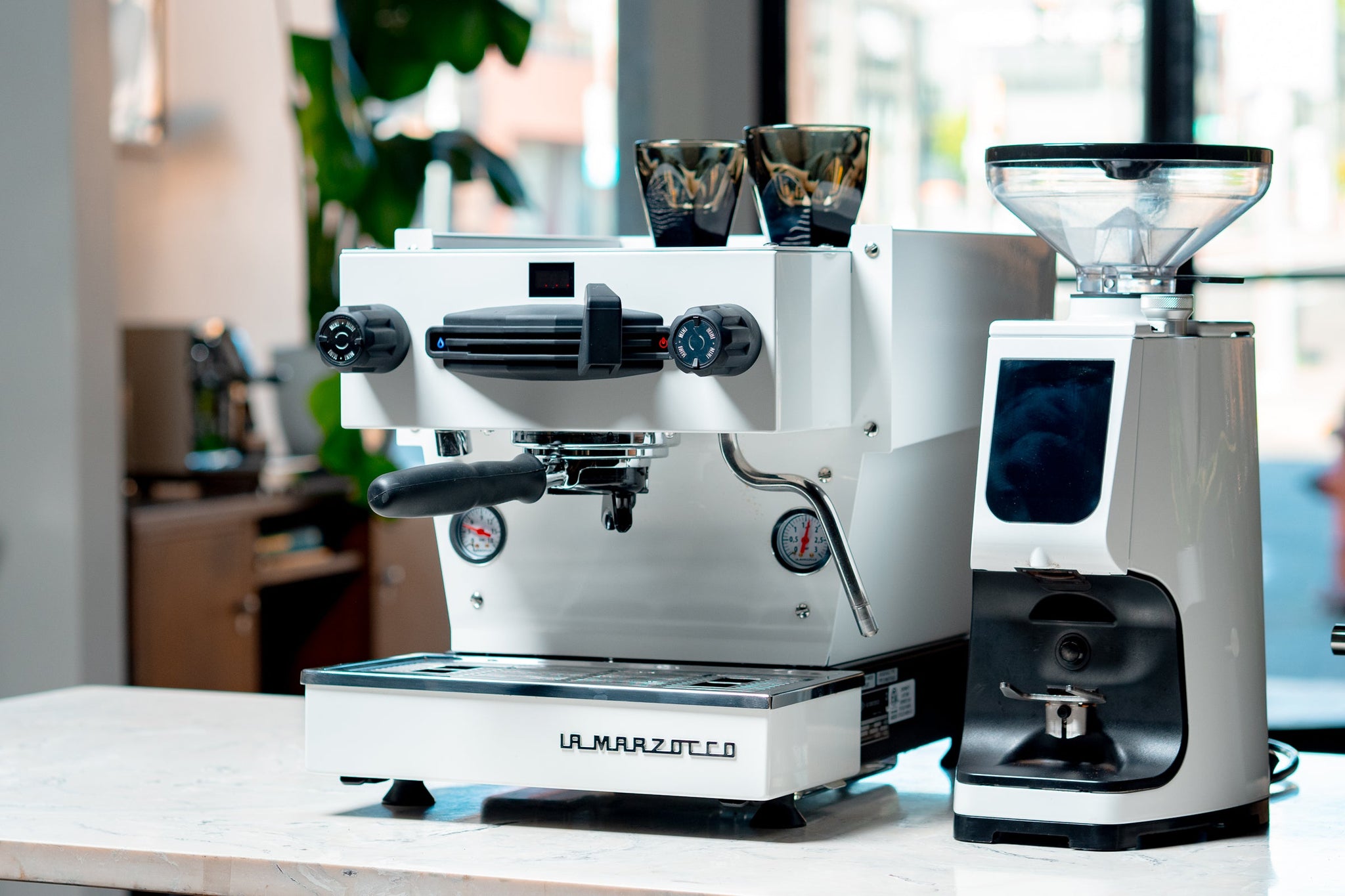 White espresso machine with a clear bean hopper on the right and La Marzocco branding on the front