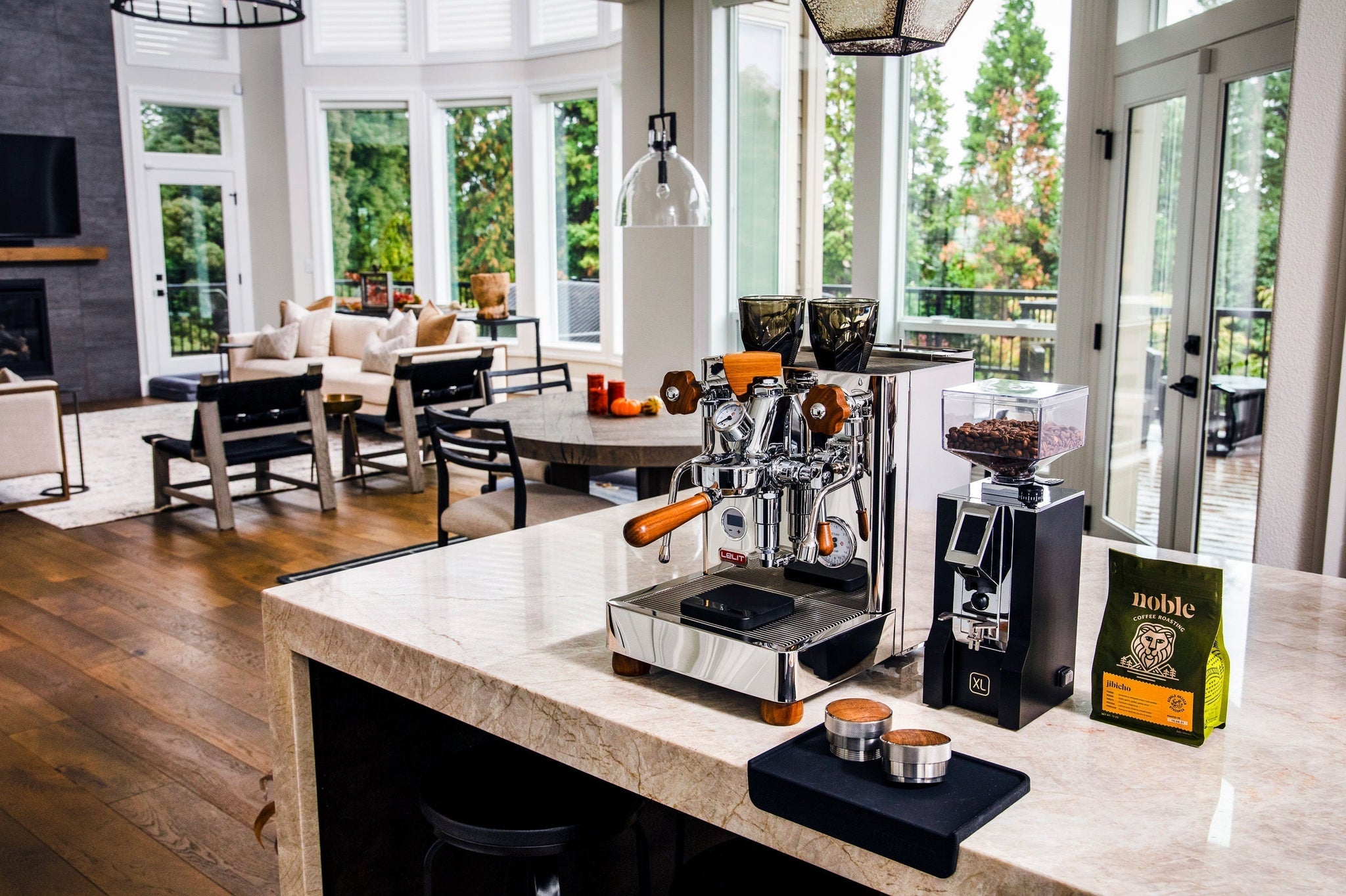 Bright kitchen with large windows featuring a polished espresso machine on a marble island and a bag of coffee