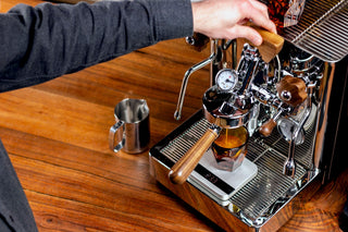 Hand on the lever of a vintage style espresso machine with a visible pressure gauge.