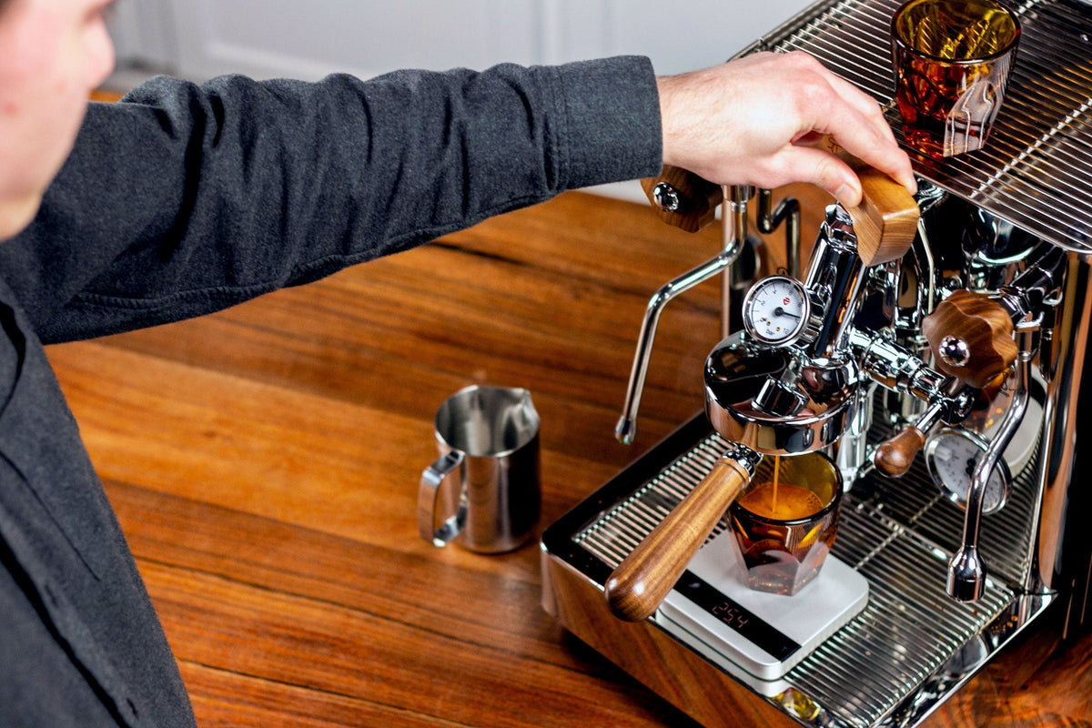 Hand turning the lever on a polished chrome espresso machine with wooden accents